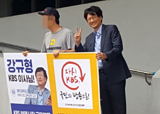 지난 2017년 9월 중순 강규형 당시 KBS 이사가 고대영 당시 KBS 사장 퇴진을 목적으로 "적폐이사회에서 물러나라"며 피켓시위를 벌이는 전국언론노동조합 KBS본부(2노조) 조합원의 바로 옆에서 환하게 웃으며 손으로 V자를 그리는 모습.[사진=KBS 2노조 페이스북]